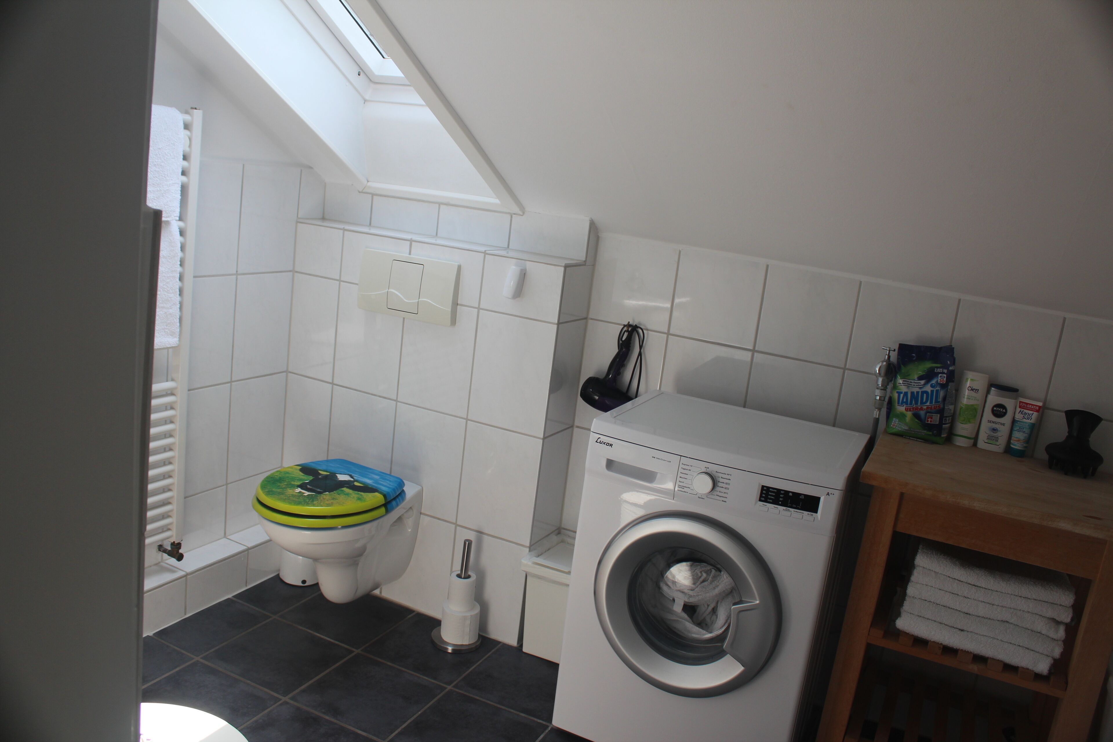 Ein kleines Badezimmer mit Toilette, Waschmaschine und einem Regal mit Handtüchern.