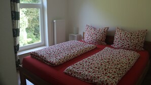 A bedroom with a bed, two pillows, a nightstand, and a window with curtains. - Charming family and pet friendly apartment in rural idyll - pure relaxation (Kiel Pries)