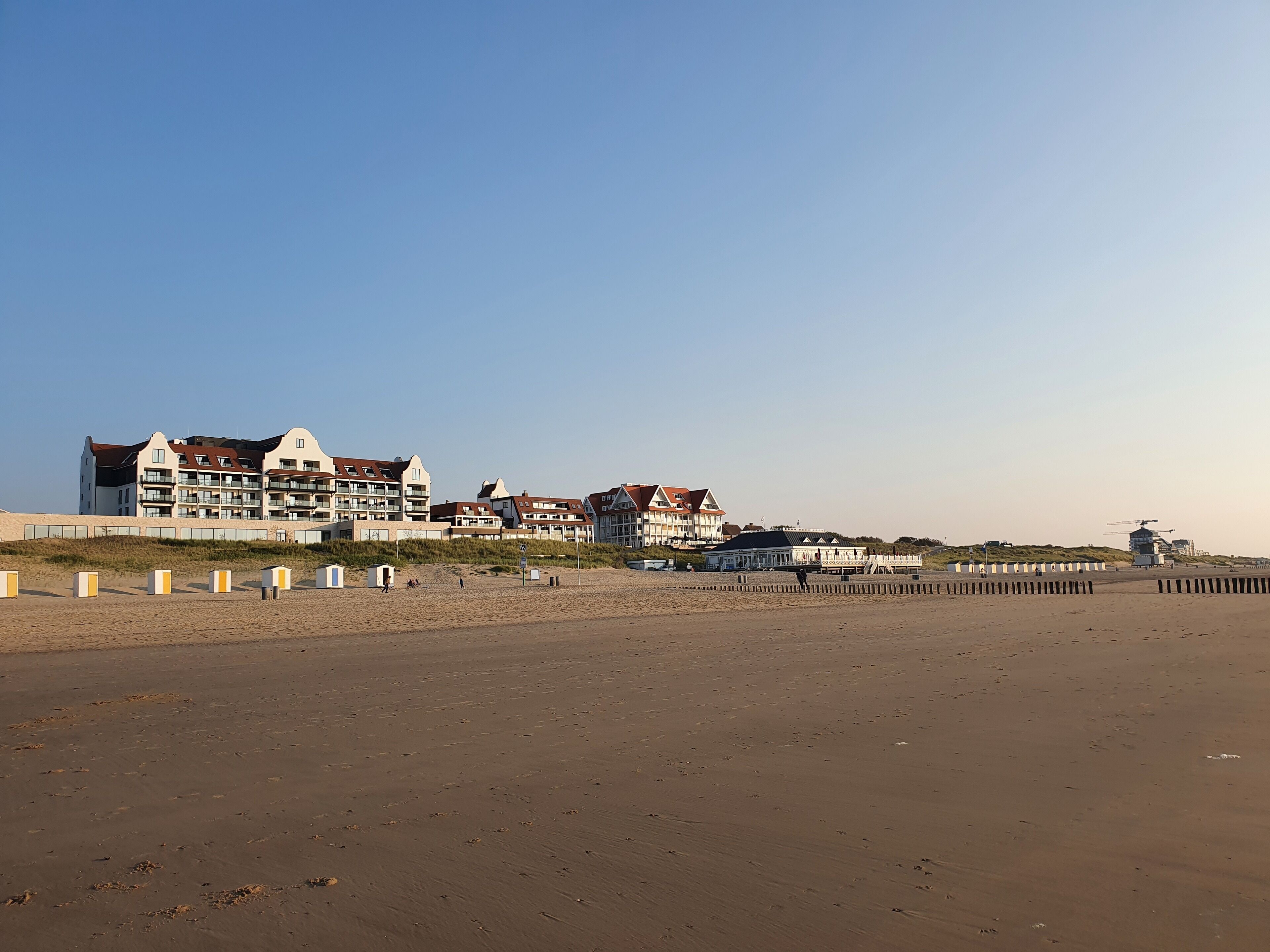 A beachfront hotel with multiple buildings, a sandy beach, and a windmill in the distance.