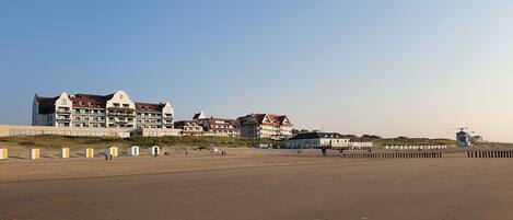 A beachfront hotel with multiple buildings, a sandy beach, and a windmill in the distance.