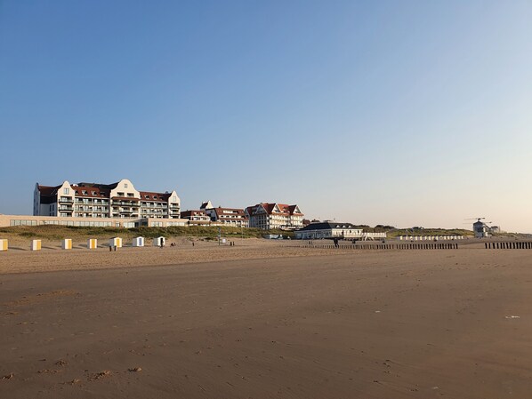 A beachfront hotel with multiple buildings, a sandy beach, and a windmill in the distance.