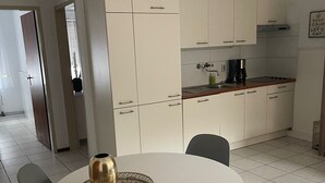 Una cocina moderna con armarios blancos, una mesa redonda con cuatro sillas y una cafetera sobre la encimera.