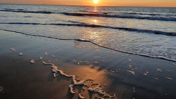 Una playa al atardecer, con olas que acarician suavemente la orilla.
