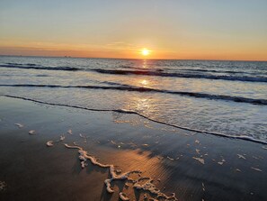 A beach at sunset with waves gently lapping the shore.
