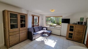 Una sala de estar con sofá, armarios de madera, televisor y ventana con vista a zonas verdes.