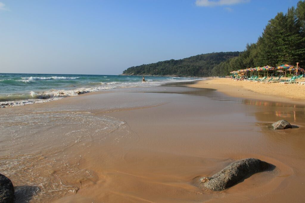 Une plage avec un ciel dégagé, une eau calme et une vue lointaine sur un paysage vallonné.