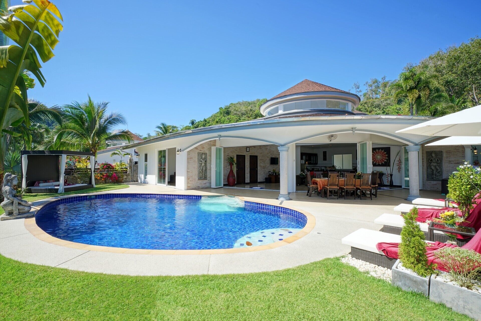 A poolside area with a circular pool, a covered patio with seating, and a house in the background.