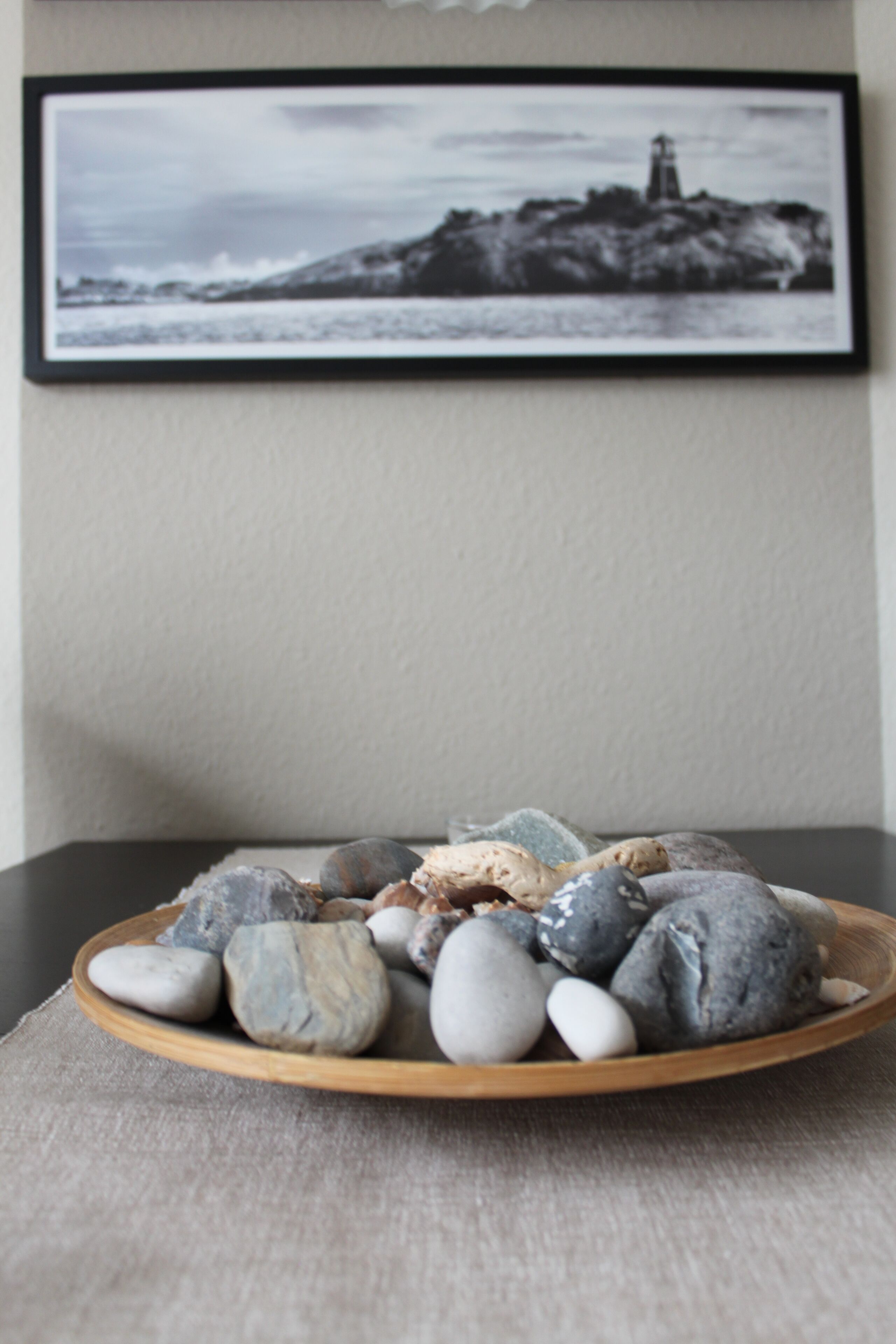 A wooden tray with smooth, rounded stones on a textured fabric surface.