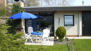 A patio with a table and chairs, a blue umbrella, and a small garden.