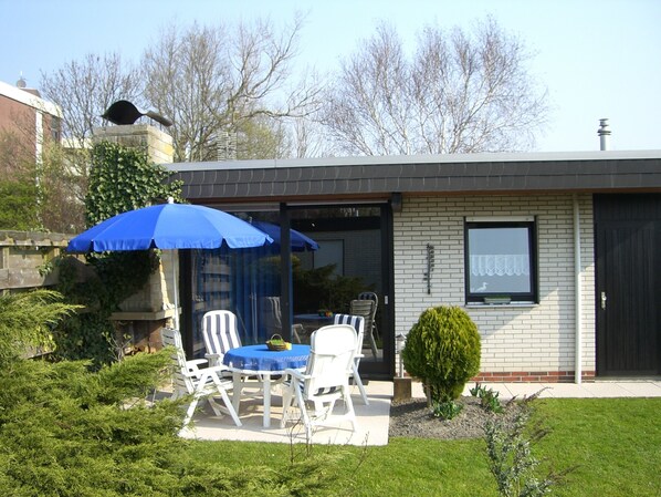 Un patio con una mesa, sillas, un paraguas azul y un pequeño jardín.