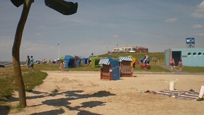 Una playa con arena, tiendas de campaña y un edificio con un letrero.