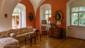 A room with a floral sofa, wooden furniture, and two large windows with arched ceilings. - Very large (105m2) family-friendly apartment in castle 'Rittergut Heyda' (Lossatal)