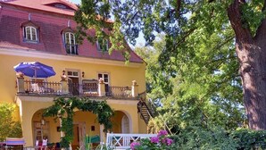 A yellow building with a balcony, surrounded by lush greenery and flowers. - Very large (105m2) family-friendly apartment in castle 'Rittergut Heyda' (Lossatal)