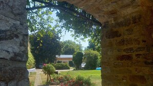 An arched stone structure with a paved courtyard, surrounded by greenery and a building in the background. - Very large (105m2) family-friendly apartment in castle 'Rittergut Heyda' (Lossatal)