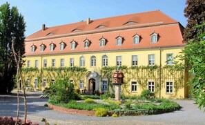 A yellow building with a red roof, multiple windows, and a garden in front. - Very large (105m2) family-friendly apartment in castle 'Rittergut Heyda' (Lossatal)