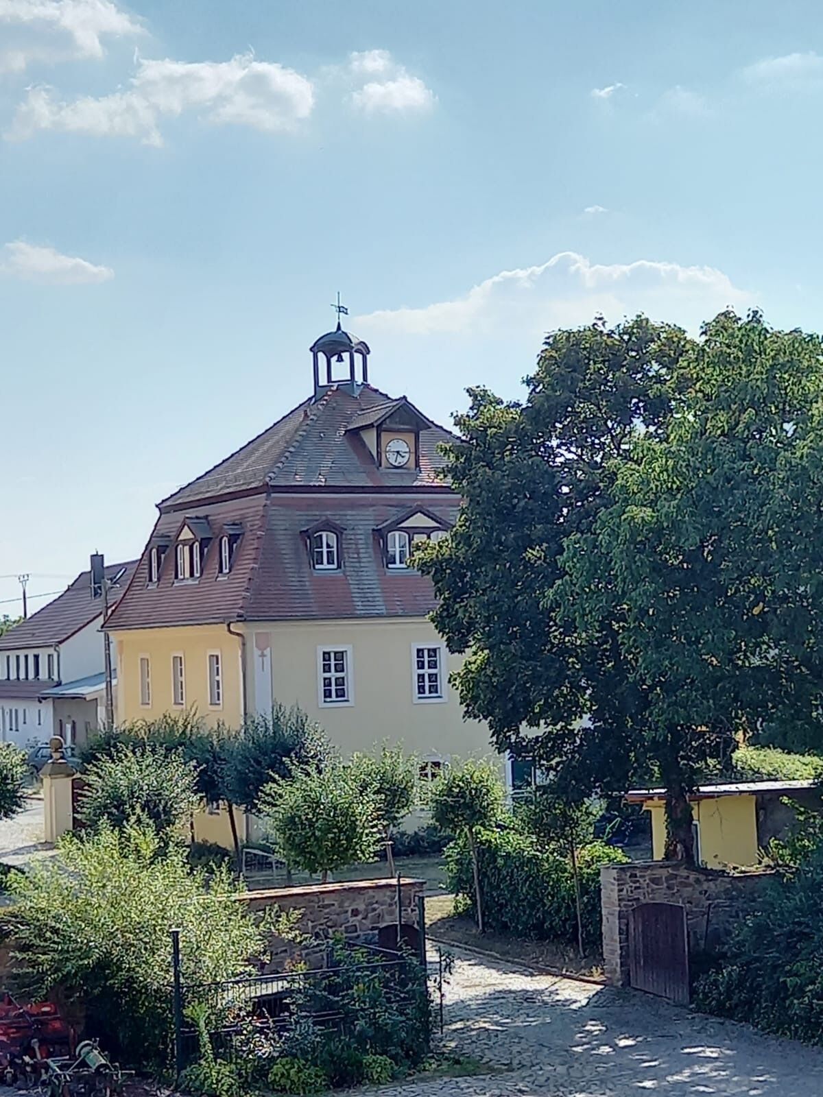 A traditional building with a clock tower, surrounded by greenery and a cobblestone path.