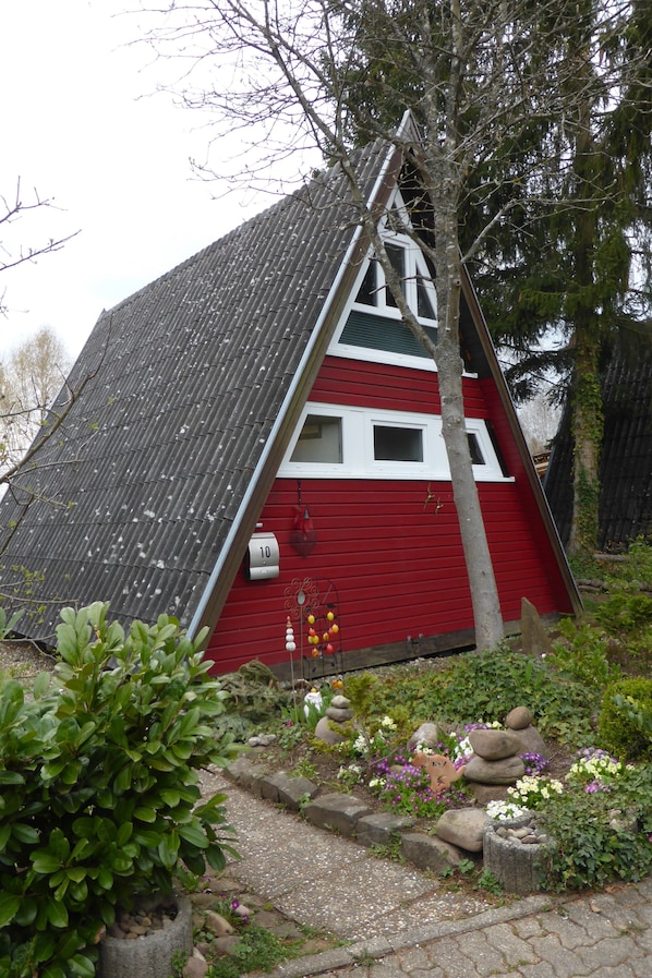 Una casa roja y blanca de techo pronunciado, rodeada de un jardín con diversas plantas y rocas.