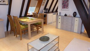 Un comedor con una mesa y sillas de madera, una pequeña zona de cocina con armarios y una encimera, y un cuadro en la pared.