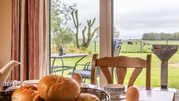 Ein Essbereich mit gedecktem Tisch für das Frühstück, einem Brotkorb und Blick auf eine Bauernhoflandschaft mit Kühen.
