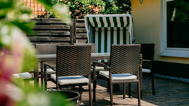 Wicker chairs and a table set up outdoors, with a wooden fence and greenery in the background.