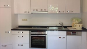 A modern kitchen with white cabinets, a stainless steel oven, and a coffee maker on the counter.