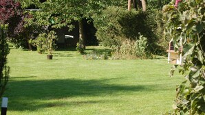 A well-maintained garden with a lawn, various plants, and a small structure.