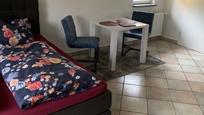 A bedroom with a bed, a chair, a small table, and a window.