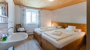 Ein Hotelzimmer mit zwei Holzbetten, einem weißen Waschbecken und einem Fenster mit floralem Vorhang.