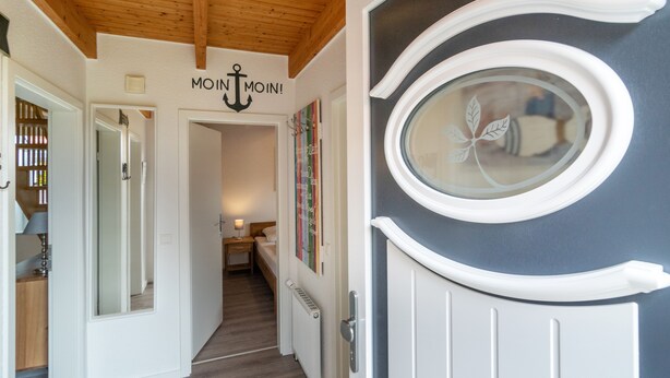 Un corridoio con soffitto in legno, una porta con finestra in vetro e un letto sullo sfondo.