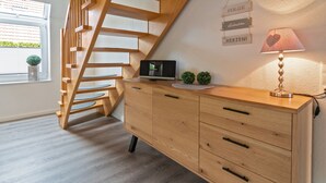 Una scala in legno conduce a una zona mansardata, un tavolo da lavoro in legno con cassetti, una lampada e una piccola pianta.