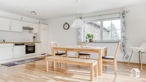 A modern kitchen with white cabinets, a wooden dining table, and a window with a view of a house.