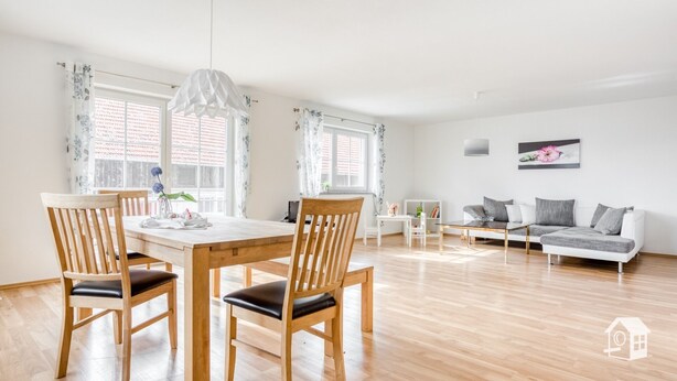 A spacious living area with a wooden dining table, two chairs, a sofa, and a coffee table.