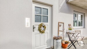 A white door with a wreath, a small table with a potted plant, and a wooden ladder leaning against the wall.