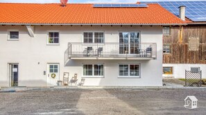 Ein zweigeschossiges Gebäude mit rotem Ziegeldach, Solaranlagen und einem Balkon mit Sitzgelegenheit.