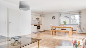 A modern apartment with a dining area, kitchen, and a large window with curtains.