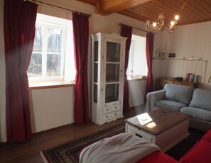 Un salon chaleureux avec un plafond en bois, une armoire blanche, un canapé bleu et un rideau rouge.