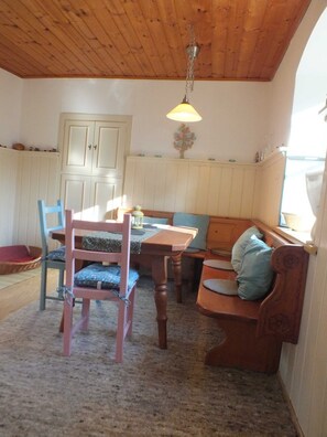 Une pièce chaleureuse avec un plafond en bois, une table à manger avec des chaises, un banc et une fenêtre avec des rideaux.