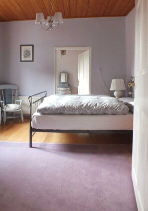 A bedroom with a bed, a chair, a dresser, and a door leading to another room.