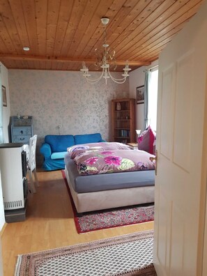 Une chambre confortable avec un plafond en bois, un canapé bleu, un lit avec une literie à motifs floraux, une bibliothèque et un tapis à motifs.