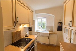Une cuisine compacte avec des meubles blancs, une cuisinière encastrée et une fenêtre qui laisse entrer la lumière naturelle.