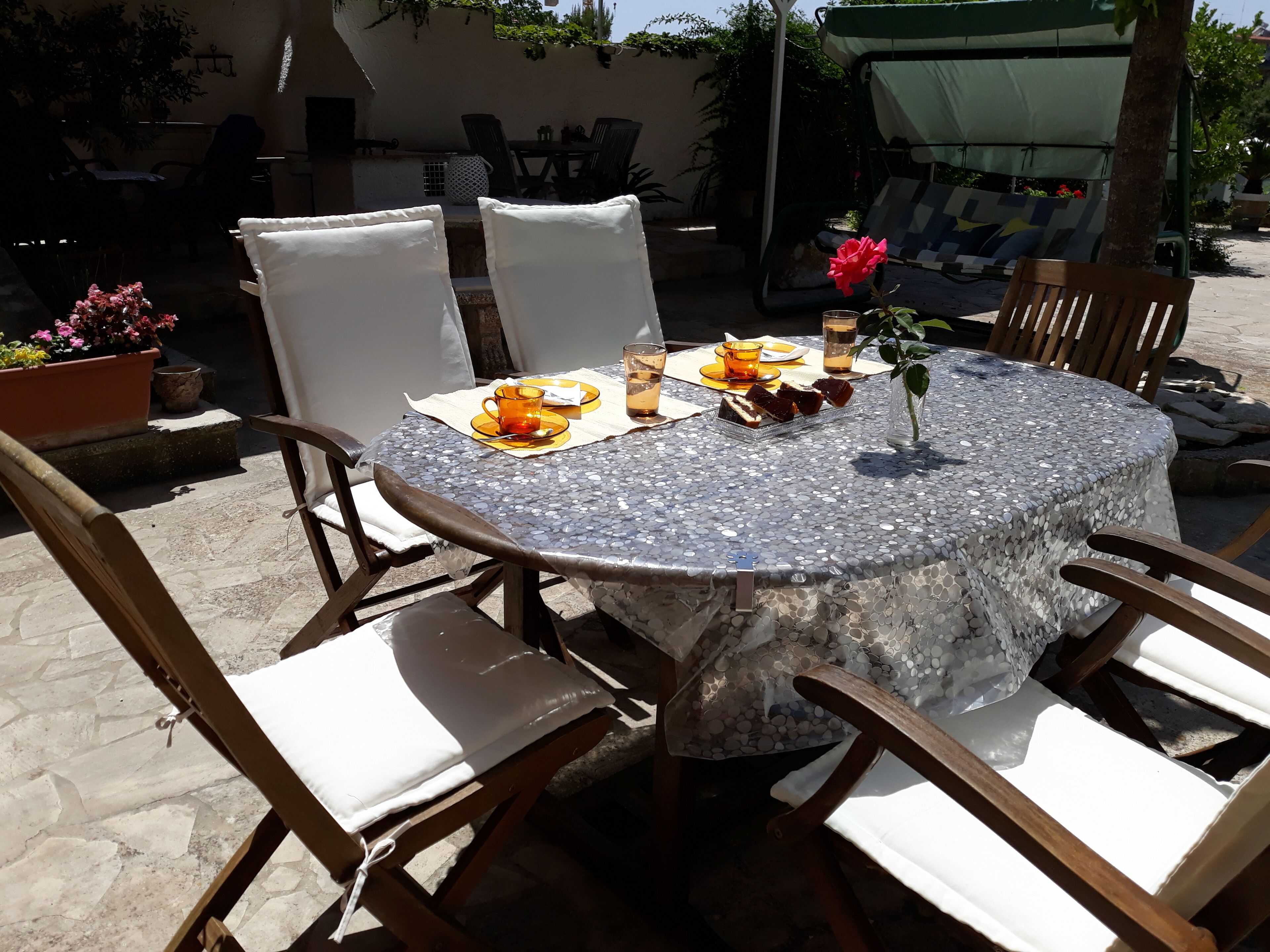 A round table with a mosaic tablecloth, surrounded by wooden chairs with white cushions.