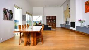 Ein geräumiges Wohnzimmer mit einem großen Holzesstisch, einem Kamin und Blick ins Freie.