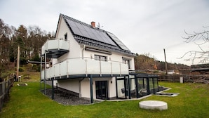 Ein modernes, zweistöckiges Haus mit Satteldach, Solaranlage, einem Glaswintergarten und einem gepflegten Rasen.
