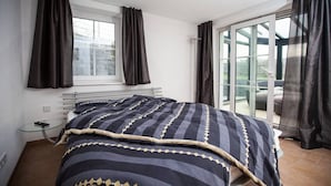 Ein Schlafzimmer mit Bett, einer Glastür, die zu einem Balkon führt, und einem Fenster mit Vorhängen.