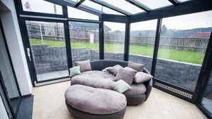 Ein sonnendurchflutetes Zimmer mit einem großen Glastür, das in einen Garten führt, mit einer runden Sitzecke mit vielen Kissen.