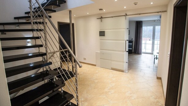Ein modernes Interieur mit einer schwarzen Treppe, einer Schiebetür und Blick auf einen Balkon.