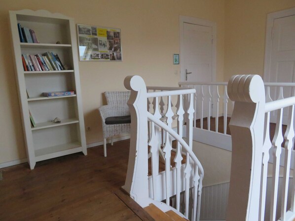 A staircase with white balusters, a wicker chair, and a bookshelf with books.