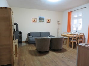 Un salon comprenant un canapé, deux fauteuils, une table à manger avec des chaises, un buffet en bois et une cheminée.