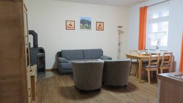 A living room with a sofa, two armchairs, a dining table with chairs, a wooden cabinet, and a fireplace.