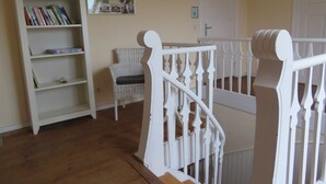 Un escalier avec des balustrades blanches, une chaise en osier et une bibliothèque remplie de livres.